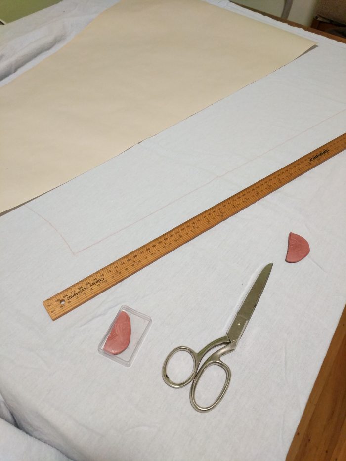 A paper pattern laid out on flannel with a line chalked. Also visible are a long ruler, a pair of fabric scissors, and tailor's chalk.