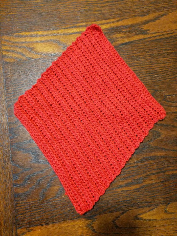 A red crochet dishcloth, in the form of a rhombus or diamond.