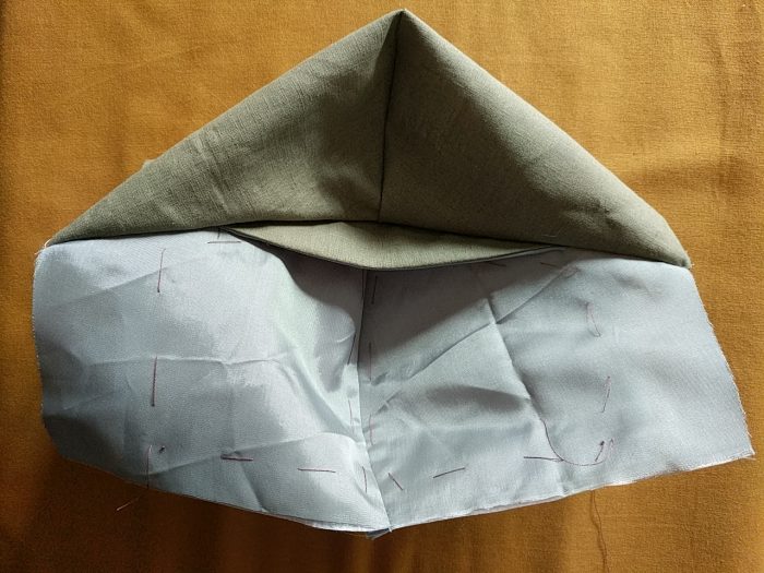 A partially completed mask. The pieces are sewn together along the top edge, and the nose piece is visible between the outer, and the inner, which has been pulled up to give this view.