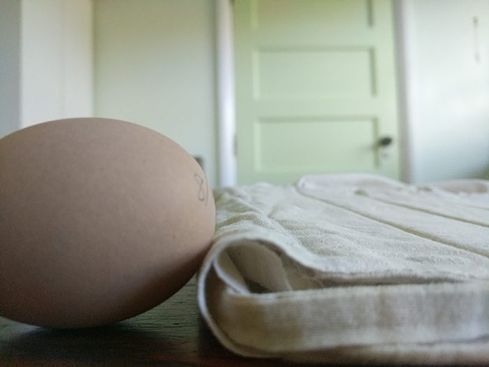 A sunbonnet, seen from the side, lies flat on a table. Next to it is an egg, lying on one side. The egg is about twice the height of the sunbonnet.