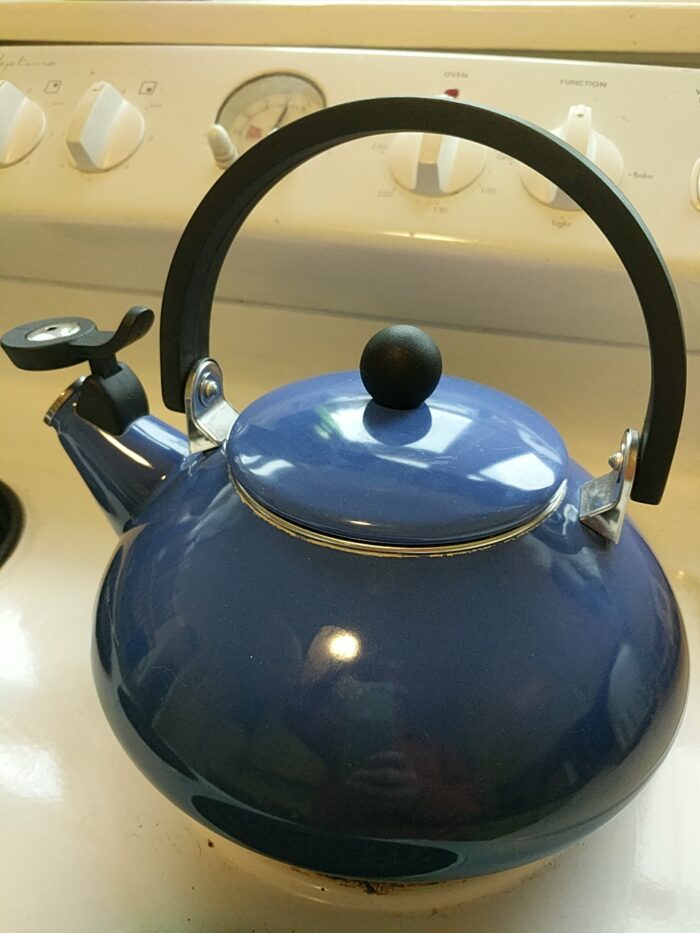 A shiny blue stovetop kettle with a black handle arching over its lid and a whistle flipped up on its spout.