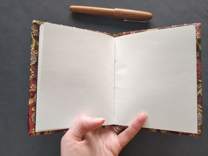 A small silk-covered book held open to show a blank spread with stitching just visible at the fold.