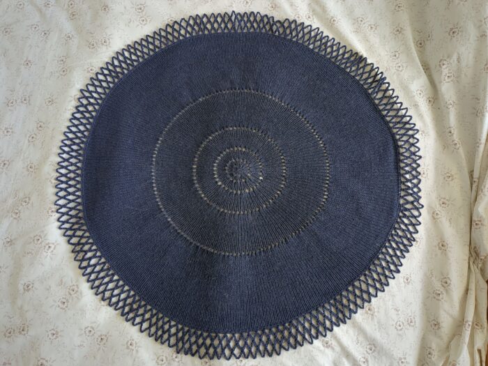 A dark blue circular shawl with circles of increases further and further apart as they move out from the centre. The edging is rather like netting.