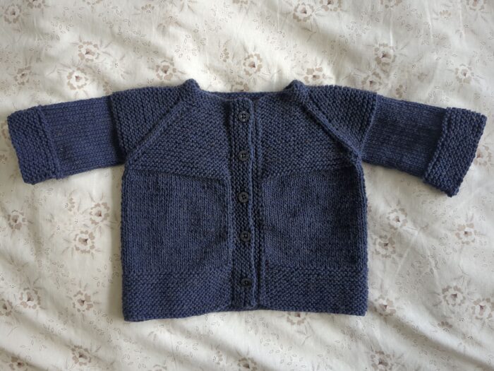 A small dark blue 8ply baby cardigan with garter stitch trimming and five buttons down the front.
