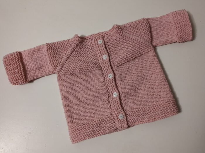 A small pink 8ply baby cardigan with garter stitch trim and five buttons down the front.