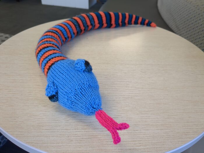A knitted snake with bright blue head and striped blue and orange body.