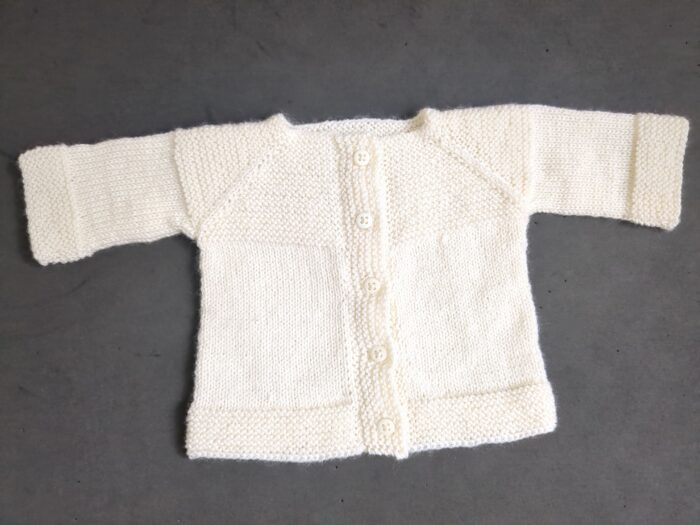 A small 3ply baby cardigan in soft cream with garter stitch trim and buttons down the front.